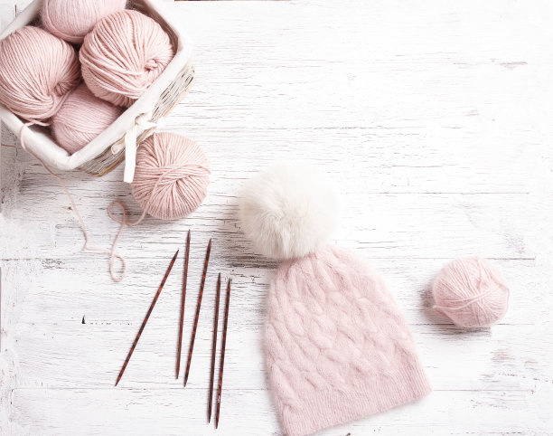 手工编织的粉红色帽子与毛皮绒球在木桌上图片下载