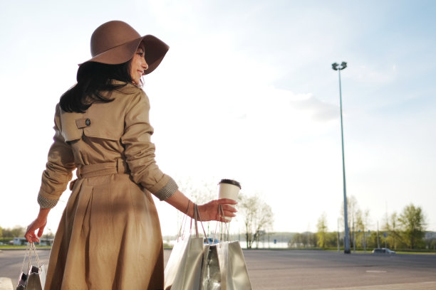 一个小女孩从购物中心走出来，手里拿着包裹和一个咖啡杯图片下载
