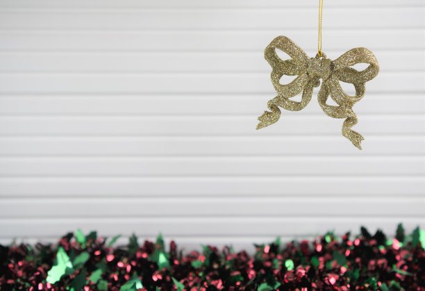 彩色圣诞摄影图片挂圣诞装饰的金色闪光弓与明亮的金丝在天然白色木材的背景图片下载