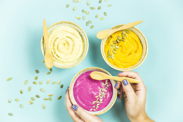 一个女人拿着甜菜根酱，旁边是鲜亮的小吃——鹰嘴豆泥和胡萝卜酱，夹在南瓜子里。前视图。平躺图片下载