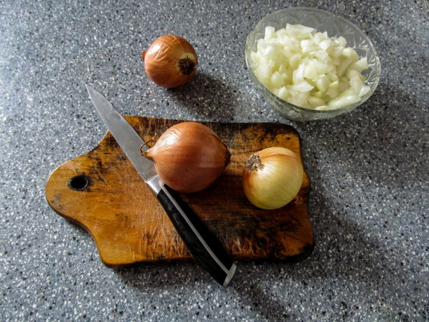 灰色的桌子上放着一个碗，里面放着三个球茎和切得很细的洋葱图片下载