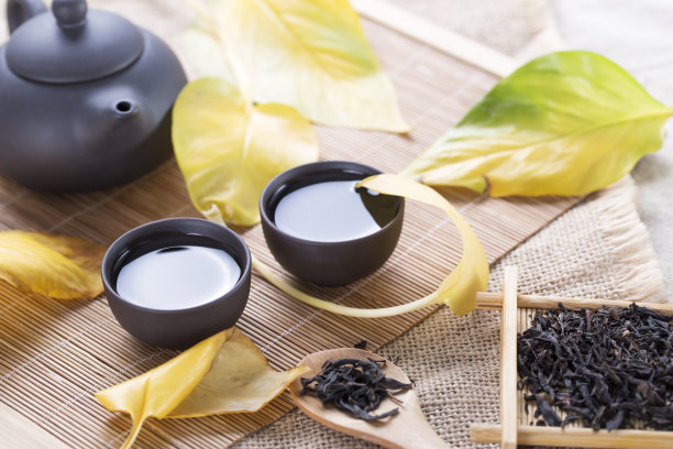 桌子上有黑色的茶壶和茶杯，上面有黄色的叶子。热饮料。秋茶。图片下载