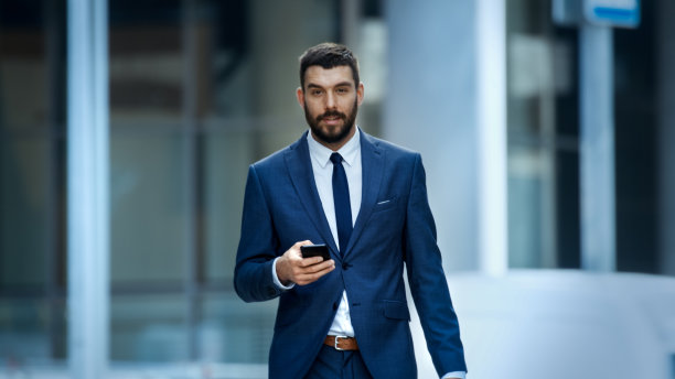 一位成功的商人在大城市商业区的街道上使用智能手机。他正对着摄像机看。图片下载