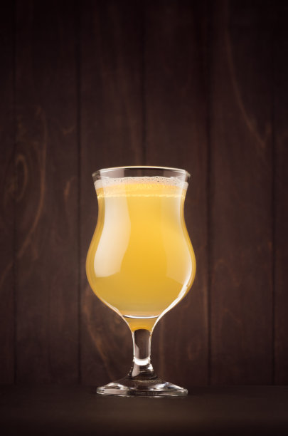 郁金香啤酒杯与泥泞的weizen在深色木板上，垂直。图片下载