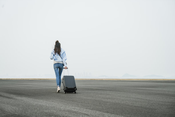 一个年轻女子拖着箱子在天空下走图片下载
