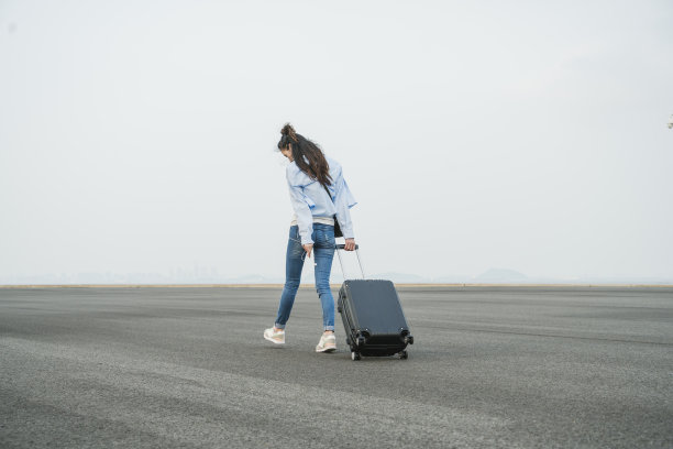 一个年轻女子拖着箱子在天空下走图片下载