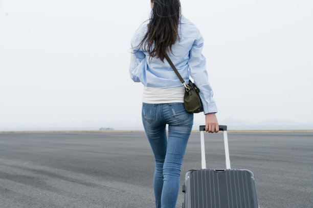 一个年轻女子拖着箱子在天空下走图片下载