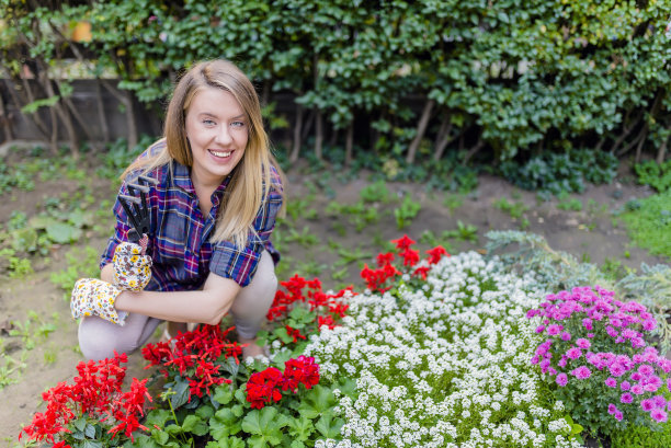 园丁在花园里照料她的植物。漂亮的女加德纳放松户外拿园艺工具。女人在花园。微笑的年轻女子照顾她的花园图片下载