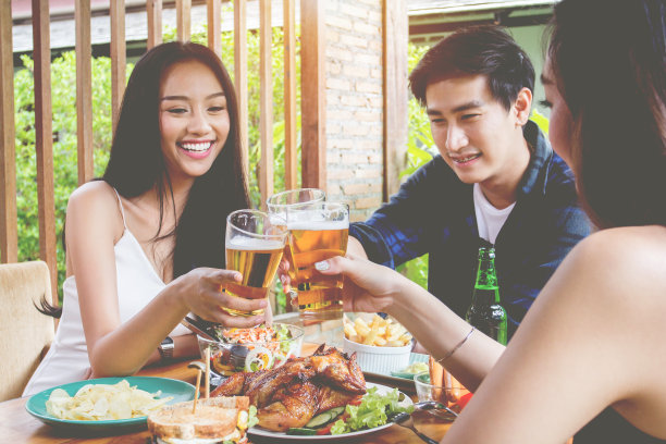 两名亚洲女子和一名男子。喝啤酒，微笑。庆祝派对，快乐饮食概念图片下载