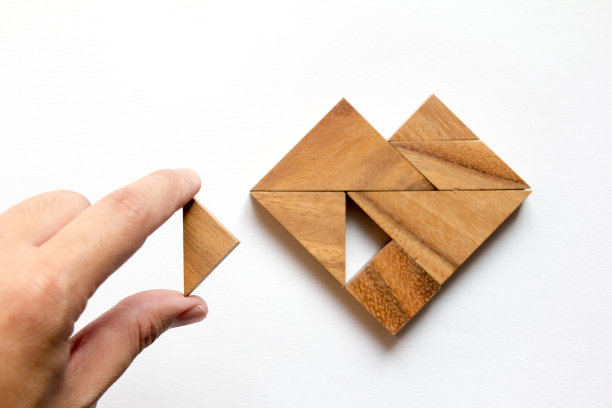 男子手持七巧板，在白色背景上拼出心形(爱的概念)图片下载