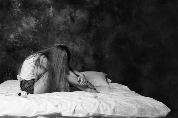 女孩沮丧地坐在床上哭泣，把脸藏在膝盖里。黑白照片图片下载