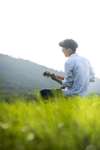 年轻男子在草坪上弹吉他的后视图图片下载