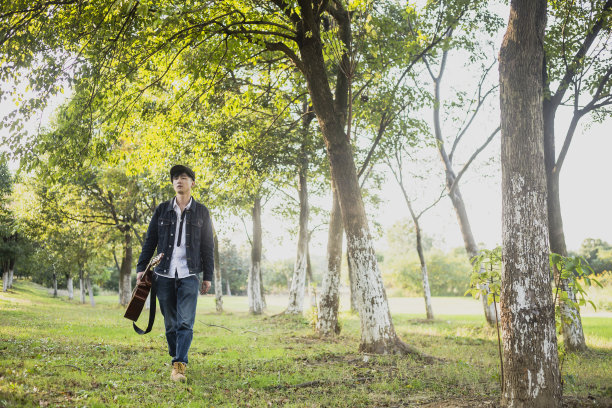 年轻人戴着平顶帽，拿着原声吉他在大自然中行走图片下载