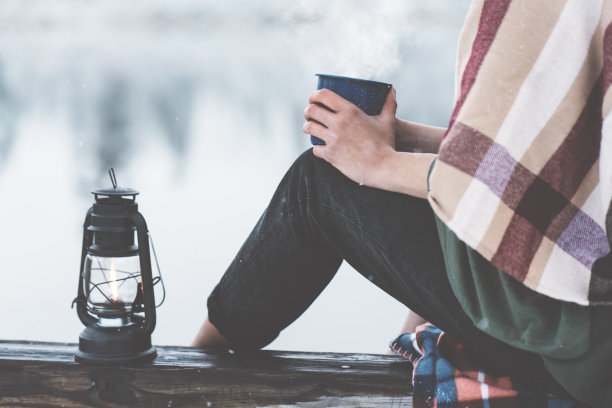 拿着热饮料和油灯的女人坐在白雪覆盖的湖边图片下载
