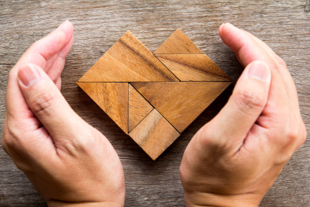 手盖七巧板拼图在心脏形状的木制背景图片下载