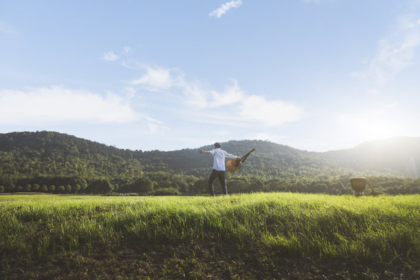 热情的年轻人拿着吉他站在草坪上图片下载