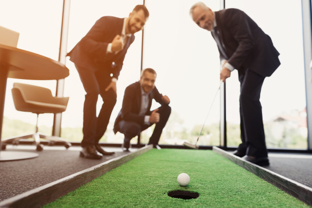一位可敬的老人正在办公室打高尔夫球。他旁边是他的工人。他们看起来像是老板在玩游戏图片下载