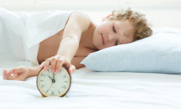 小男孩躺在床上，停止闹钟在早上。图片下载