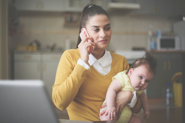 快乐的妈妈抱着她的小宝贝在家里讲手机。图片下载