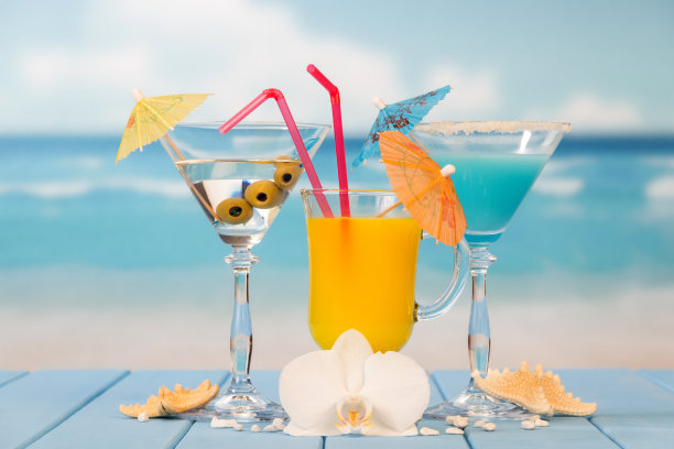 鸡尾酒，一杯果汁和酒精与橄榄，雨伞和吸管，海星，贝壳和兰花对着大海。图片下载