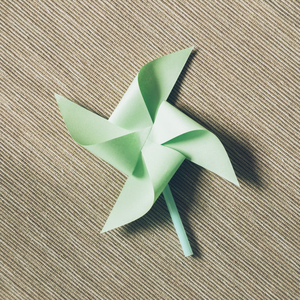 绿色纸风车在棕色织物的背景图片下载