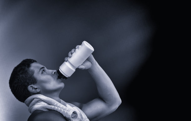 年轻的肌肉男在跑步或户外工作后喝瓶装水。健身和健康生活理念。孤立在黑色图片下载