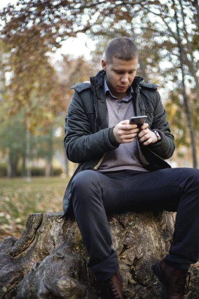年轻英俊的男子在秋季公园使用智能手机图片下载