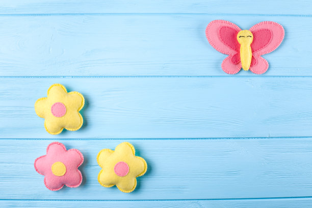 用白色的纸制作粉色和黄色的蝴蝶和花朵，蓝色的木制背景上的拷贝空间。手工制作的毛毡玩具。抽象的天空。图片下载