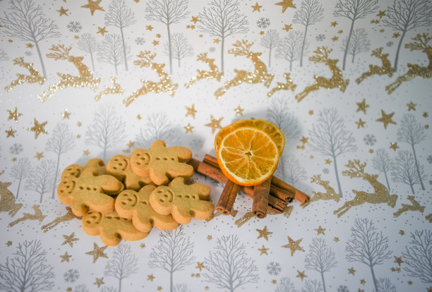 彩色圣诞食物图片姜饼人饼干与肉桂香料和橙色水果片和驯鹿金色闪闪发光的包装纸背景图片下载