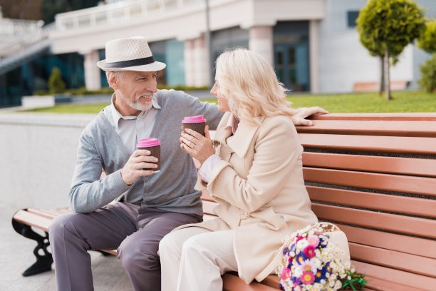 两个退休老人坐在长凳上，手里拿着一杯咖啡。他们温柔地看着对方图片下载