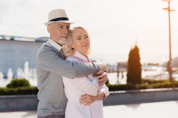 一对老夫妇正在广场上散步。他们微笑着拥抱着站在那里图片下载