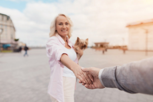 一对老夫妇正在广场上散步。女人牵着男人的手，领着他图片下载