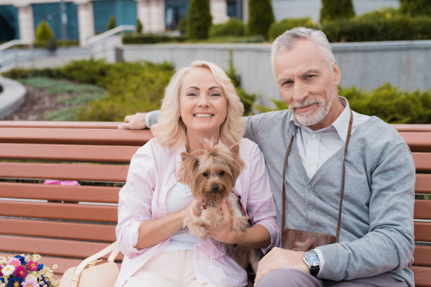 一对老夫妇坐在广场的长凳上休息。一位妇女有一只漂亮的小狗坐在她的手上图片下载
