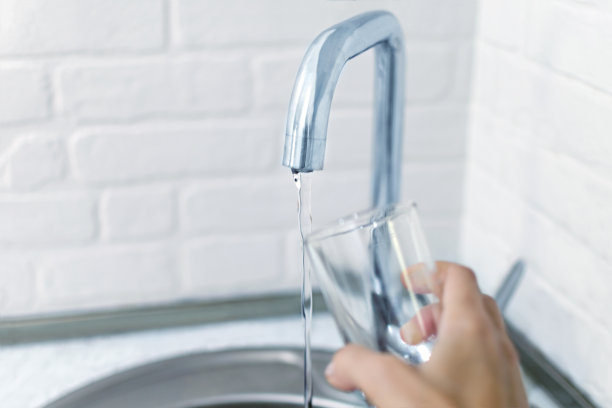 女人的手把杯子举向水龙头的喷水口。照片与中空深度的焦点。图片下载
