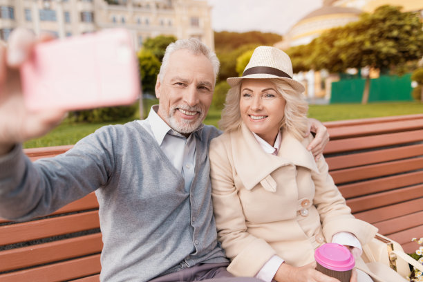 两个退休老人坐在长凳上，手里拿着一杯咖啡。他们坐着拥抱自拍图片下载