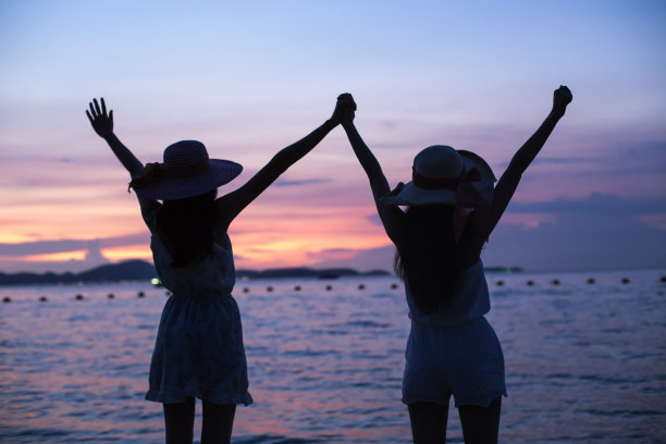 肖像的幸福年轻的亚洲妇女手握她的朋友在海滩。人们在一起享受，照片有剪影的风格。图片下载