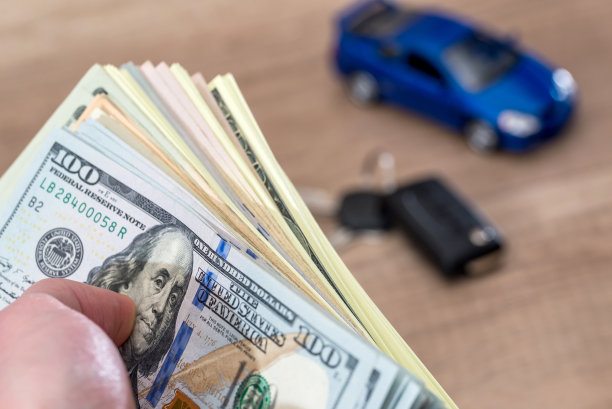 木制桌子上放着带钱和车钥匙的蓝色玩具车。图片下载