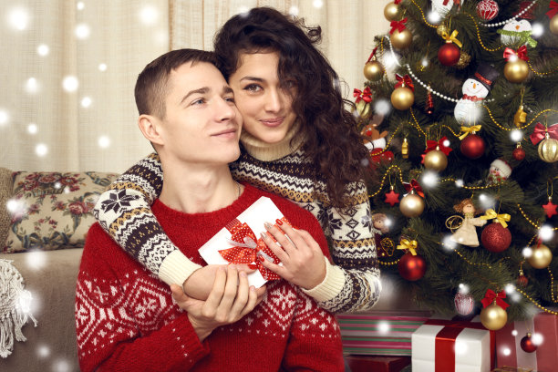 快乐的夫妇在家里给圣诞装饰礼物。除夕之夜，装饰冷杉树。寒假和爱情概念。图片下载