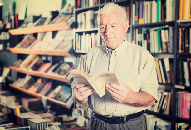 一位老人正在挑选空闲时间阅读的书图片下载