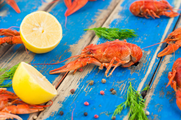 把整只煮熟的小龙虾、小茴香、两半新鲜柠檬和胡椒撒在粗糙的旧木板上图片下载