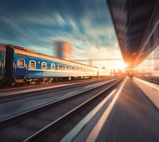 日落时分，美丽的火车和蓝色的车厢在火车站的运动。工业视图与现代火车，铁路，铁路站台，建筑物，多云的天空与运动模糊效果。概念图片下载