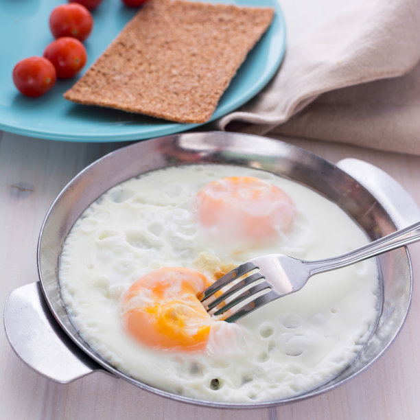 美味的煎蛋在煎锅里。开胃的早餐。煎蛋。我把蛋黄粘在叉子上。蓝色盘子里的圣女果。模糊的背景。美丽的图片。图片下载