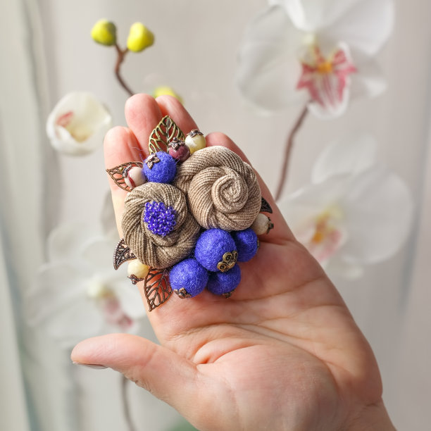 一名妇女的手掌上放着两枚米黄色花朵形状的手工小胸针图片下载