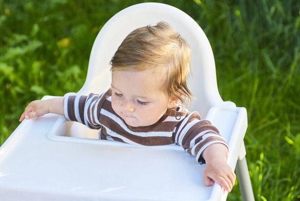 金发小女孩饭后坐在儿童高椅上，手里拿着一瓶水，笑着。图片下载