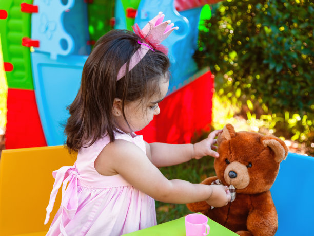 蹒跚学步的小女孩在户外的茶会上给她最好的朋友泰迪熊吃橡皮糖。图片下载
