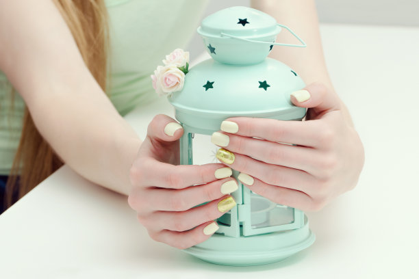 漂亮的女性手美甲和灯光背景上的烛台。金黄色的指甲图片下载