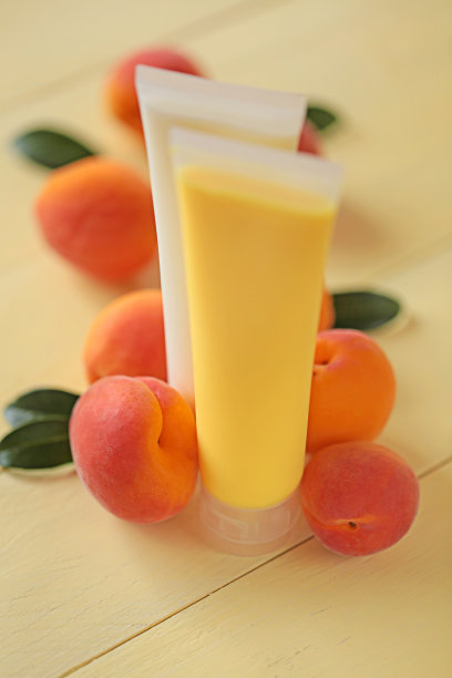 杏子提取物化妆品。黄色杏子沐浴露和白色身体霜，杏子提取物和杏子水果在黄色木质背景。有机化妆品图片下载