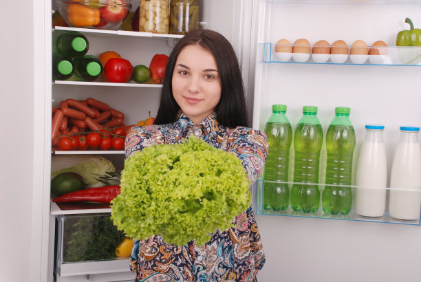 冰箱旁边有漂亮的年轻女孩，吃着健康的食物。图片下载