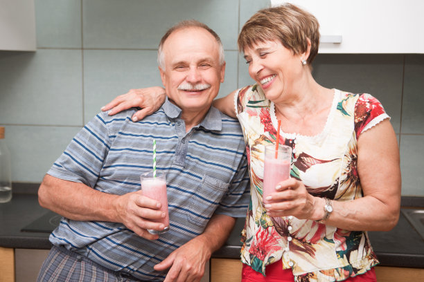 快乐的老年人拿着杯子与健康的自制水果饮料新鲜冰沙在厨房图片下载
