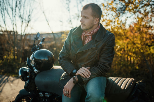 摩托车手坐在一辆旧的咖啡赛车上，背景是秋天图片下载